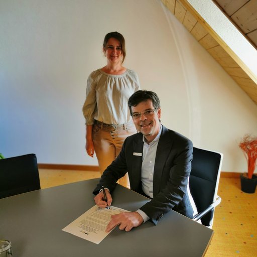 Herr Bürgermeister Georg Riedmann bei der Unterzeichnung der unterstützenden Erklärung zum Klimaschutzpakt Baden-Württemberg, im Hintergrund die städtische Energie- und Klimaschutzmanagerin Frau Eva Glöggler